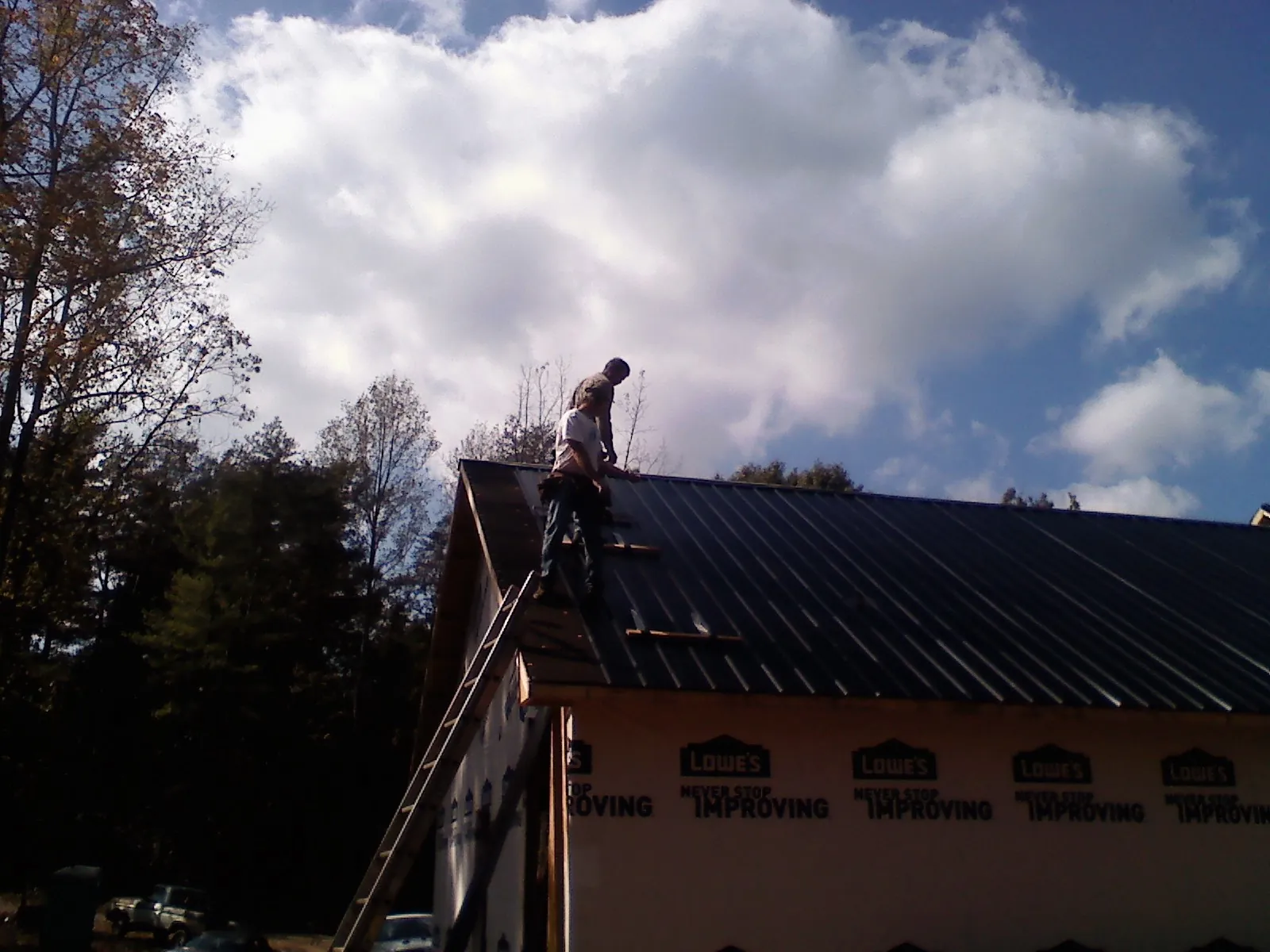 Roofer fastening dark metal panels high against a cloudy sky, from a Roof Inspection job in Eagle Lake