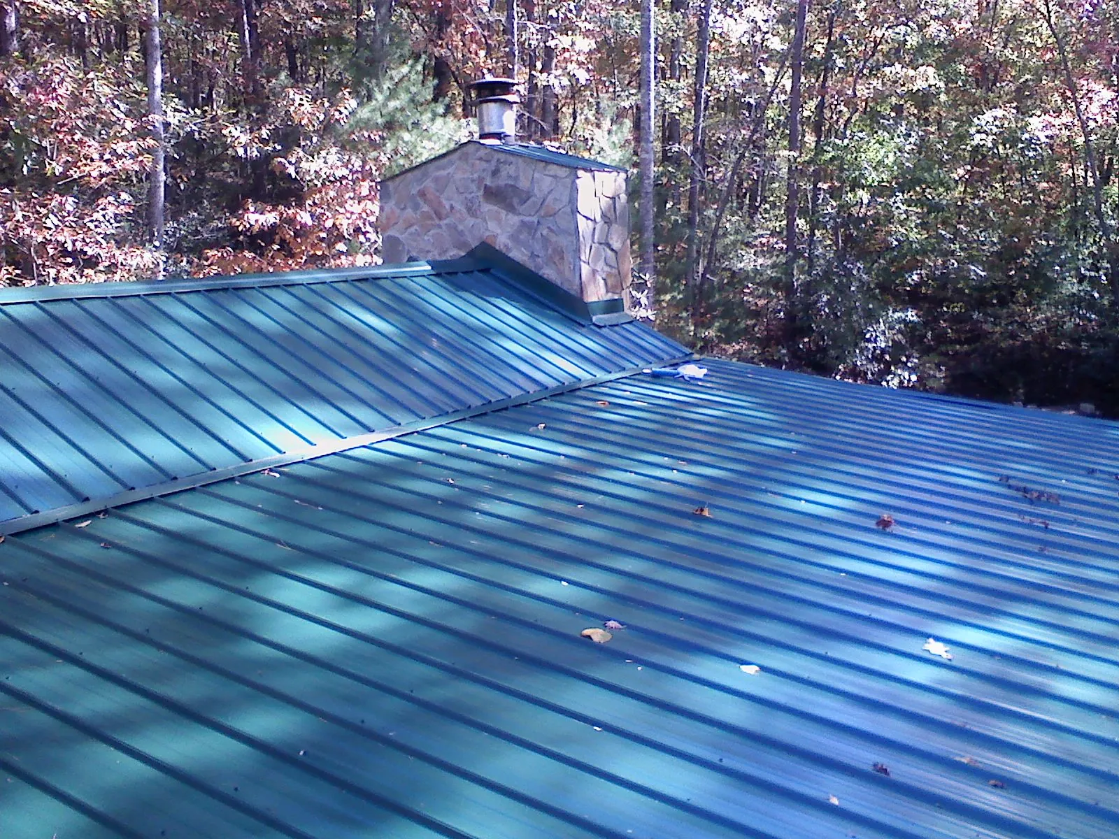 New green metal roof and stone chimney surrounded by autumn woods in Eagle Lake
